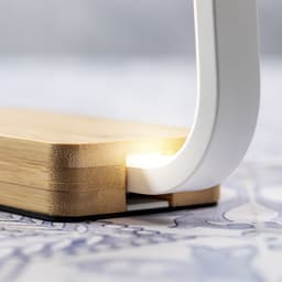 A wireless charger lamp with a sleek white design and a bamboo base, emitting a soft glow.