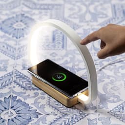 A wireless charger lamp with a white arch design and a wooden base, featuring a phone charging underneath.
