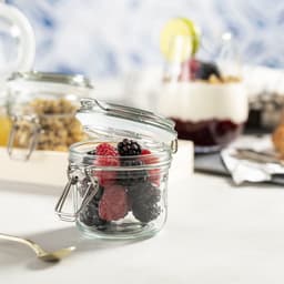 A glass jar filled with fresh berries, featuring a metal clasp lid and a transparent design.