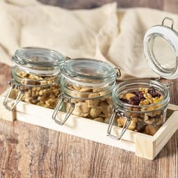 A set of three glass jars with metal clasps, filled with nuts and mounted on a wooden tray.