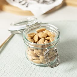 A glass jar with a metal clasp filled with light brown snacks, sitting on a textured surface.