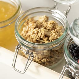 A glass jar filled with granola, featuring a metal clamp lid, beside other jars of preserves and fruit.