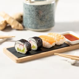 A Gunkan sushi set featuring assorted sushi rolls on a black slate plate with a side of soy sauce and ginger.