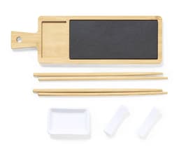 A bamboo sushi serving board with a black stone section, chopsticks, and small white dishes.