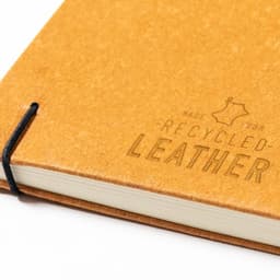 A notebook with a recycled leather cover in a warm, tan colour, featuring an elastic band closure and branding.