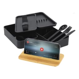 A black lunch box with compartments, cutlery, and a bamboo phone stand. The lid is partially open, revealing inside items.