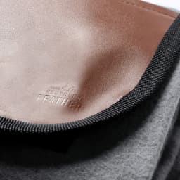 A grey and brown blanket featuring a leather detail and a logo, made of soft, textured materials.