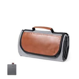 A grey picnic rug with a brown leather handle and a folded design. It has a logo on one side.