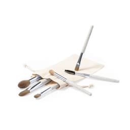 A set of makeup brushes in various sizes, featuring white handles and silver accents, placed beside a natural fabric pouch.