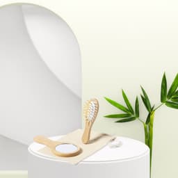 A bamboo hairbrush and hand mirror set, displayed on a cloth with green leaves in the background.