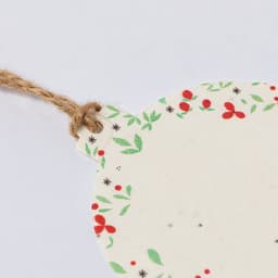 A decorative seed tag with a floral design, featuring red berries and green leaves, attached to a jute twine.