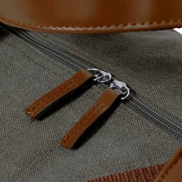 A close-up of a green bag featuring brown leather zipper pulls and a smooth zipper. The bag has a textured surface.