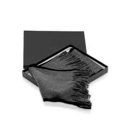 A dark grey scarf with fringed edges, presented in a sleek black box. The product has a branding label.