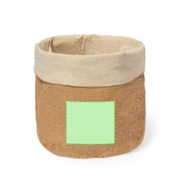A round, natural jute bread basket with a beige fabric rim and a blank green patch. It has a simple, rustic design.