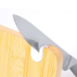 A wooden chopping board with a knife partially inserted, showcasing its bamboo texture and a small cutout feature.