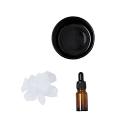 A black bowl, an amber dropper bottle, and a pile of white crystals arranged neatly.