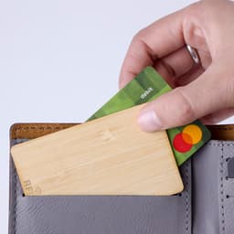 A bamboo card being inserted into a grey wallet, with a debit card visible beside it. The wallet has a minimalist design.