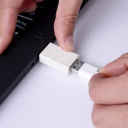 A USB drive with a textured white casing is being plugged into a laptop's USB port.