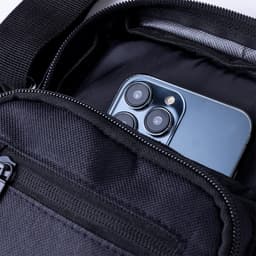 A black bag with a zipped pocket containing a smartphone, showcasing a sleek design and sturdy material.