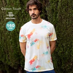 A man wearing a short-sleeved white T-shirt with a multicoloured splash pattern, standing against greenery.