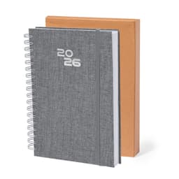 A grey diary with a spiral binding and 2026 embossed, set against a brown cardboard box.
