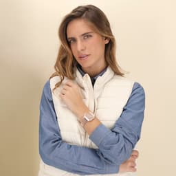 A woman wearing a silver Busnor Clock watch on her wrist, dressed in a light vest over a blue shirt.