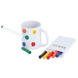 A white mug with smiley face stickers, accompanied by a green marker and a set of coloured markers in red, yellow, black, and blue.