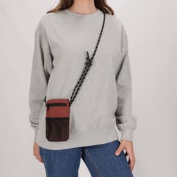 A grey sweatshirt paired with a crossbody bag in brown and black with a mesh panel, featuring a logo.