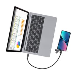 A grey laptop connected to a phone via a charging cable. A secondary screen displays graphs and data.