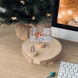 A wooden photo holder with two slots for pictures, featuring a tree and star design, set on a desk with a Christmas theme.