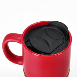 A red travel mug with a black lid, featuring a smooth design and a sturdy handle. It has a logo on the side.