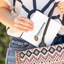 A patterned bag featuring pink, blue, and cream colours, with a person placing a white item inside. The item has a logo.