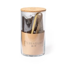 A glass terrarium kit featuring soil, pebbles, and tools, with a cork lid and a branded label.