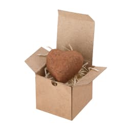 A heart-shaped chocolate truffle inside an open kraft box, surrounded by shredded paper.