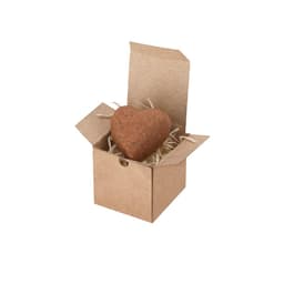 A heart-shaped chocolate truffle in a small, open brown cardboard box with straw filling. The box has a rustic appearance.