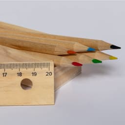 A set of wooden pencils in red, green, yellow, orange, and black, positioned next to a wooden ruler.