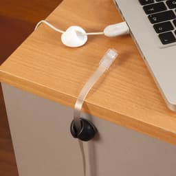A black cable tidy sits on a wooden desk, holding a clear cable in place next to a laptop.