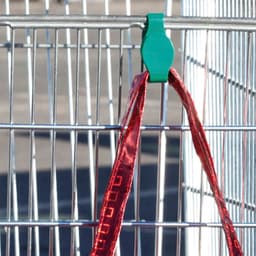 A red bag with a shiny finish is clipped to a wire cage with a green plastic hook.