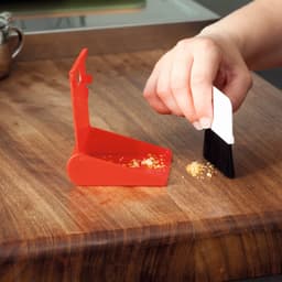 A red dustpan and brush set being used to clean crumbs from a wooden surface.