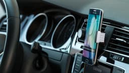 A black car phone holder securely mounted on a dashboard, holding a smartphone in place with a silver interior.