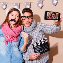 A novelty photo set featuring a couple with props like a fake moustache and glasses, holding a clapperboard and posing for a selfie.