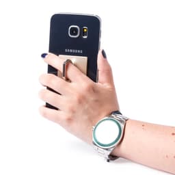 A hand holding a black Samsung phone equipped with a metallic holder, wearing a silver watch. The image features a logo.