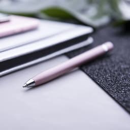 A pink ballpoint pen with a silver clip, positioned beside notebooks and a textured black surface.