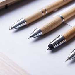 Wooden pens in a natural finish with silver accents, displayed on a white surface. Features logos on some pens.
