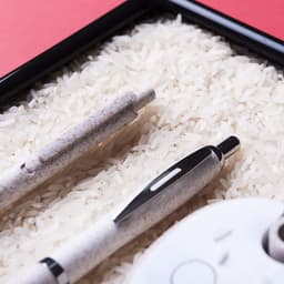 Two pens, one grey and one white, positioned on a bed of white rice in a black tray.