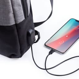 A grey and black Versox bag with a USB port, connected to a smartphone via a charging cable.