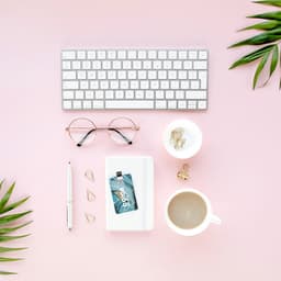 A 16Gb USB drive in a white case, surrounded by a keyboard, glasses, coffee cup, and plants on a pink surface.