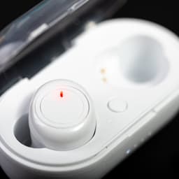 A pair of white earbuds in a charging case, featuring a red indicator light and a logo on the lid.