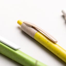 A yellow pen with a beige clip alongside a green pen and a white pen, all with branding.