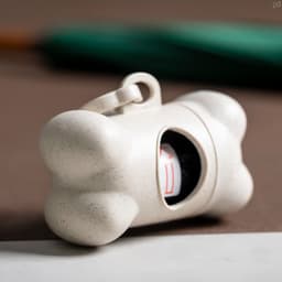 A beige bone-shaped pet accessory with a compartment, featuring a logo on the side.